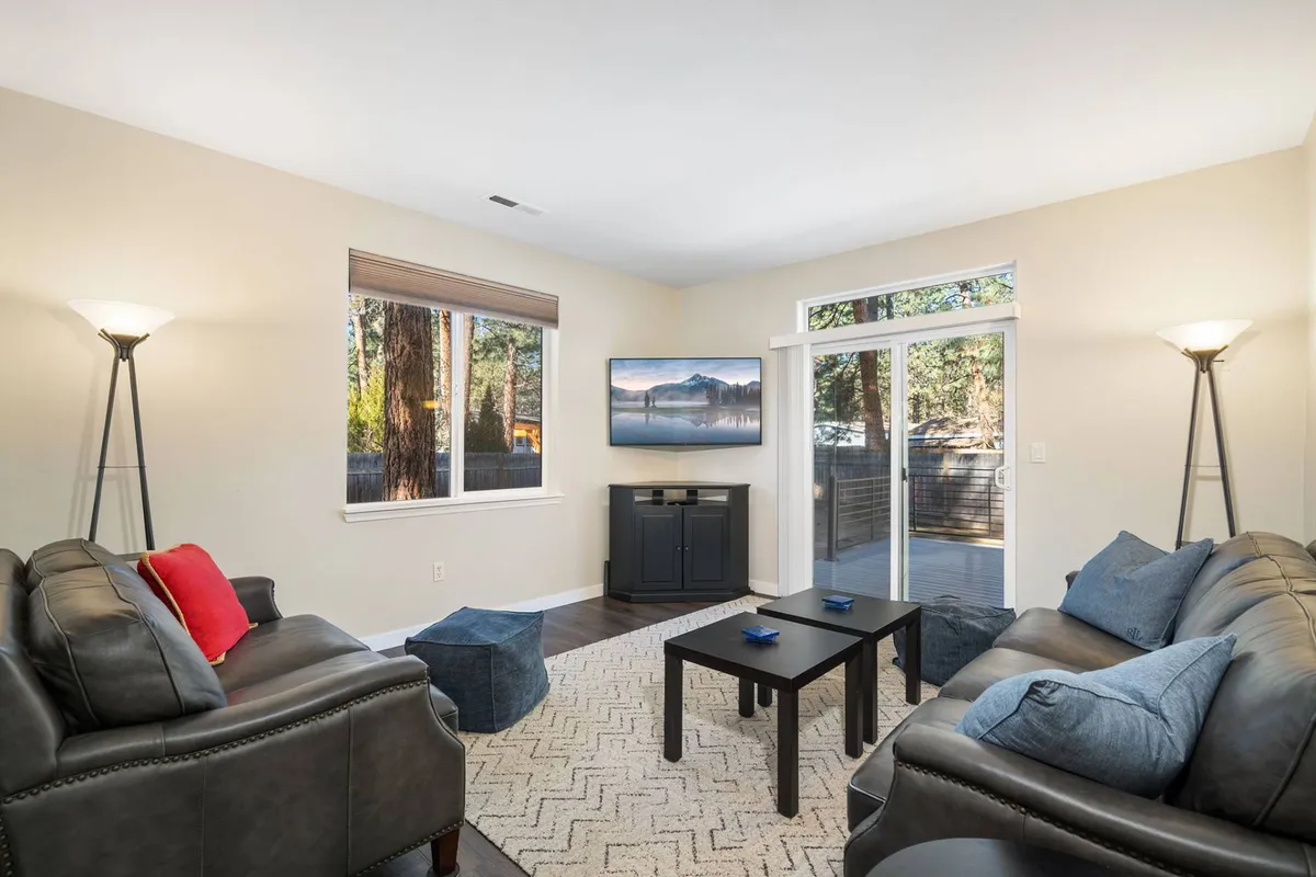 The image showcases a warm, inviting living room with plush sofas arranged around a stylish coffee table, a large television, and expansive windows letting in natural light and offering serene views. The setting feels perfect for cozy gatherings, family movie nights, or simply relaxing while taking in the peaceful surroundings.