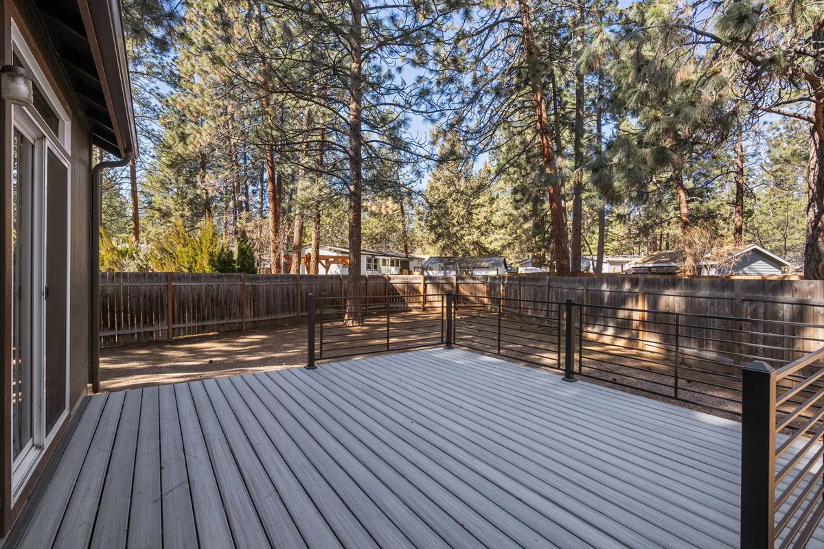 A spacious wooden deck opens onto a fully fenced backyard, bordered by mature trees that offer privacy and a sense of calm. The deck features ample space for seating and entertaining, while the surrounding foliage frames the outdoor living area, making it inviting in every season.