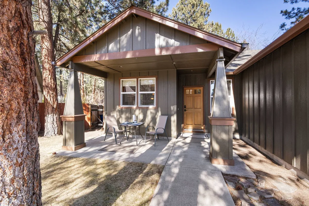 This exterior image shows a welcoming front porch with a table and chairs, perfect for gathering with friends. The entrance door is visible, offering a glimpse into the home's inviting atmosphere and highlighting the transition from the vibrant Bend scene back to a relaxing home base.