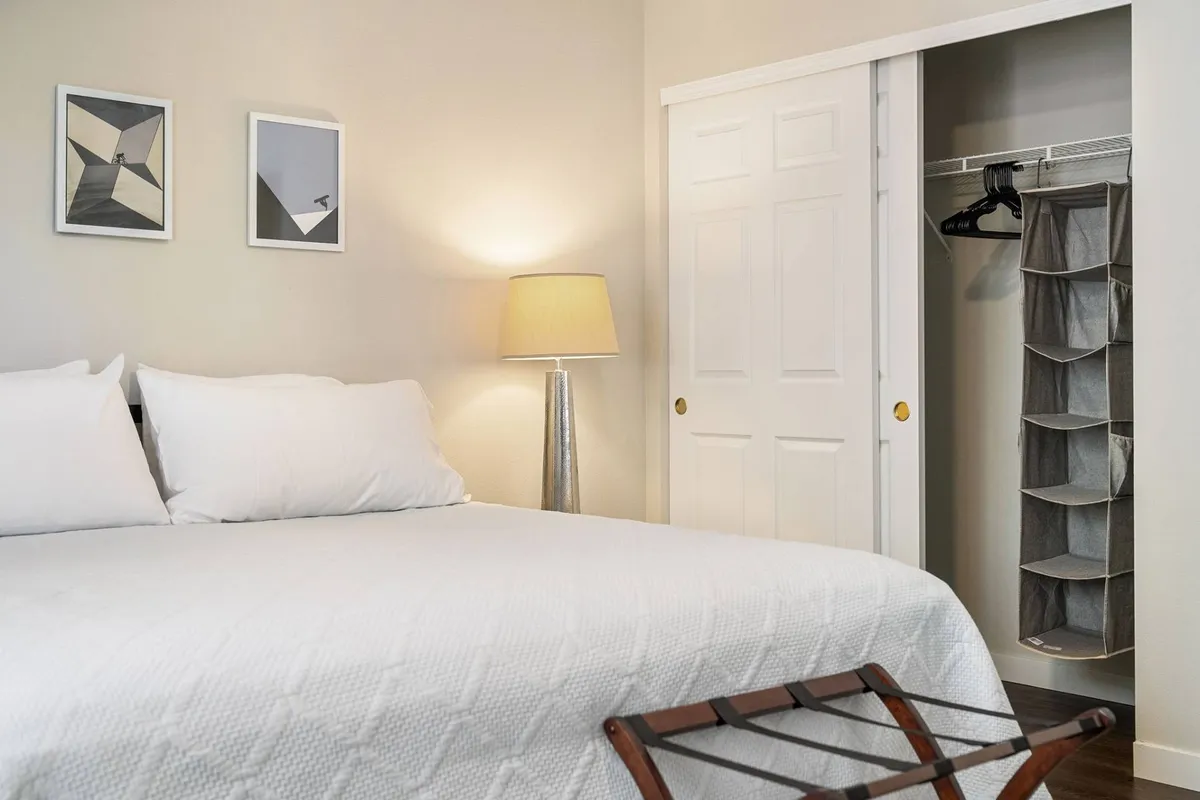 A serene bedroom featuring a cozy bed with soft linens, a bedside lamp casting gentle light, tasteful artwork on the wall, and a spacious closet. The atmosphere is tranquil and inviting, ideal for relaxation after an active day.