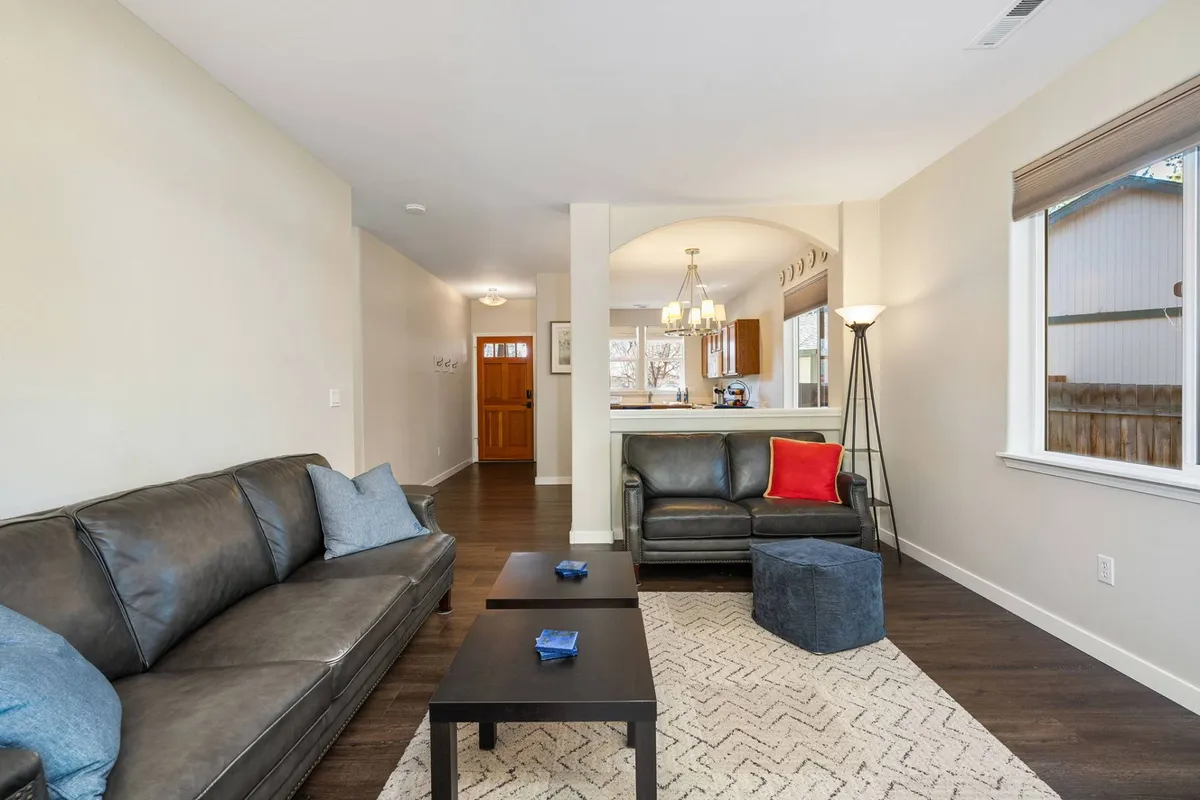 A comfortable living room featuring plush sofas, decorative cushions, coffee tables, and a warm lamp. The space is designed for relaxation and socializing, with ample seating for family and friends and a sense of openness created by the arrangement of furniture and natural light.