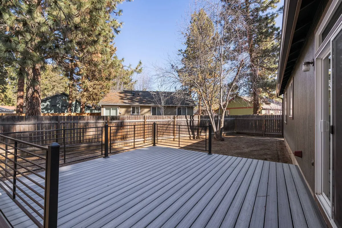 A tranquil view from the deck, bordered by a sturdy railing and surrounded by mature trees. The backyard offers space for gathering or quiet reflection, with golden sunlight filtering through the leaves—ideal for outdoor relaxation in warm weather.